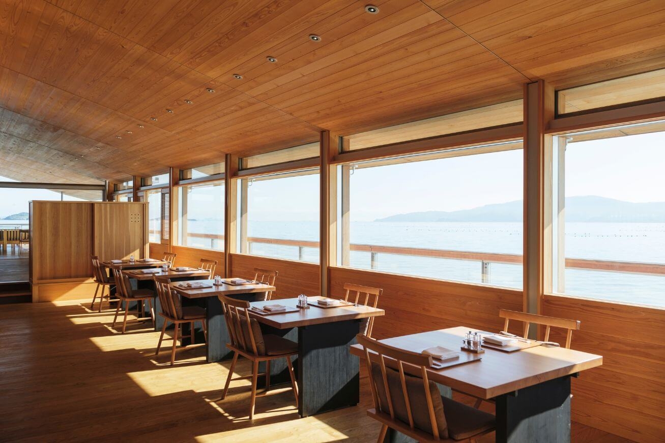 A wood-panelled dining room with several tables set for two and panoramic sea views