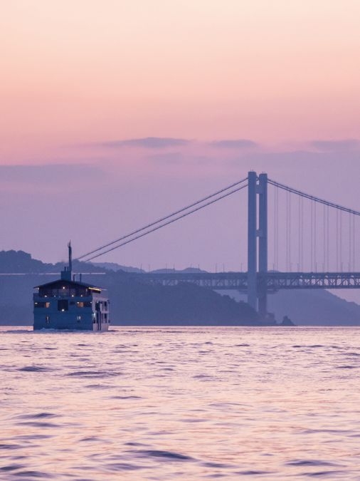 Wide view of the guntû cruise ship at sunset with a bridge in the background