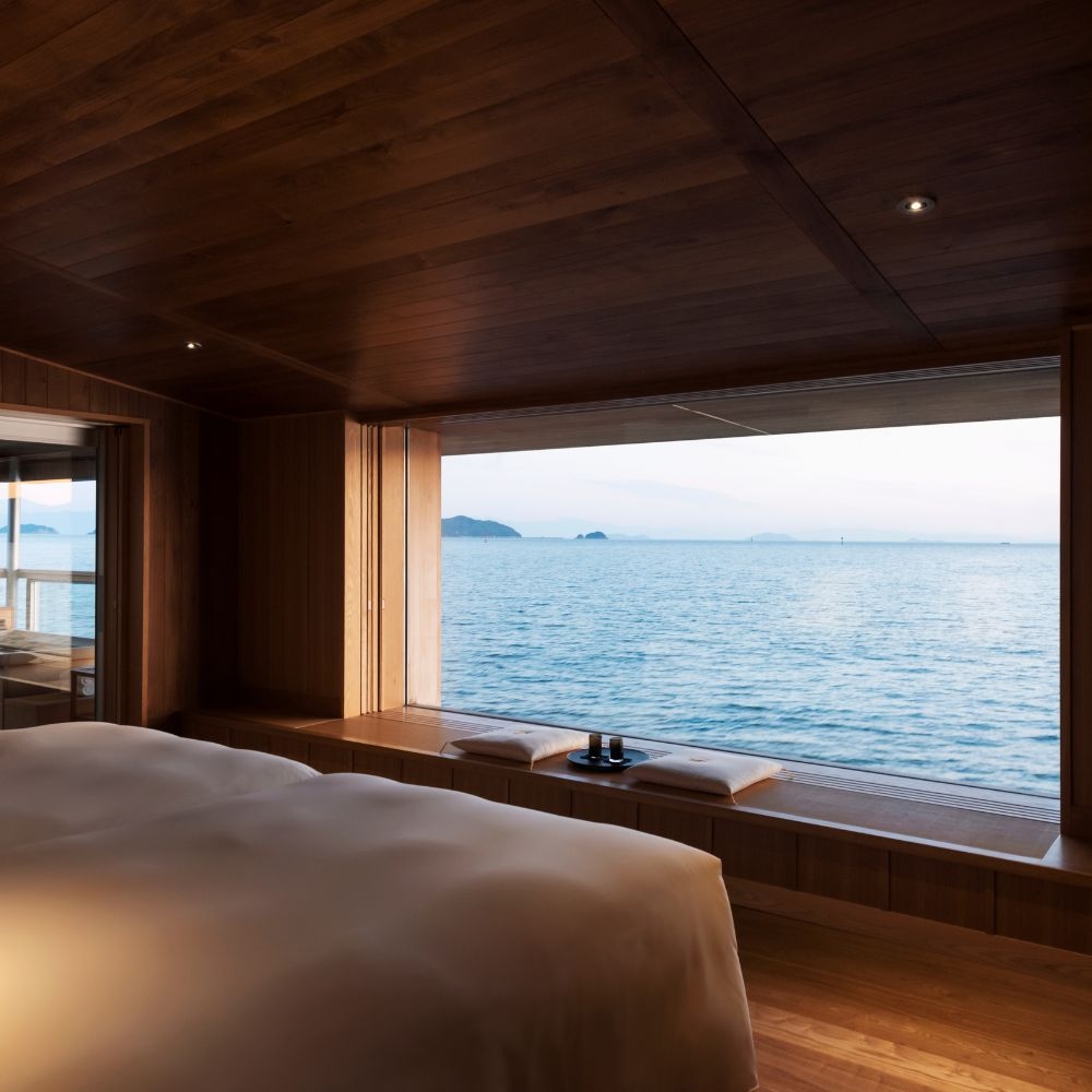 A ship cabin with a bed and bench overlooking a large window with a sea view