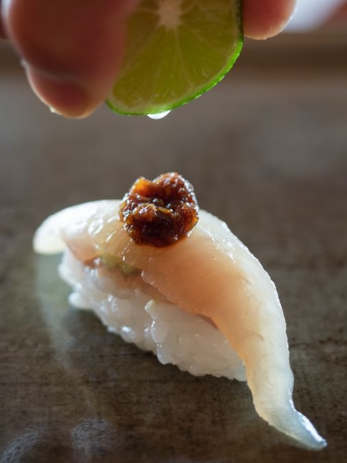 Close-up of sashimi with someone squeezing a drop of lime juice onto it