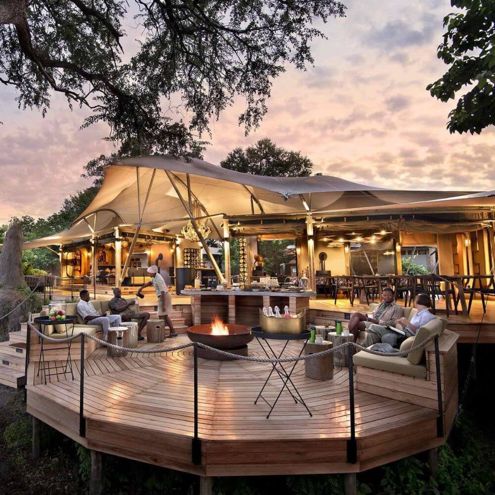 A raised round wooden deck with people sitting around a fire pit