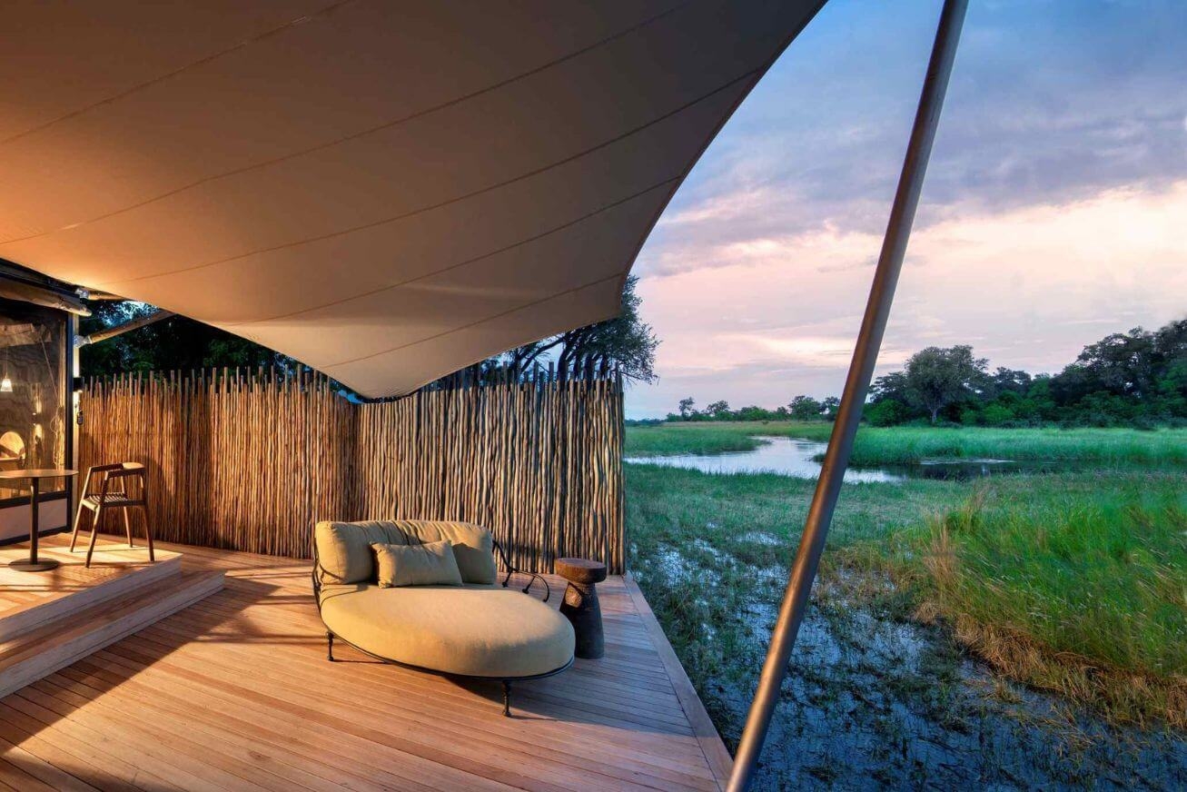 Covered wooden deck with a lounge chair overlooking a river at sunset