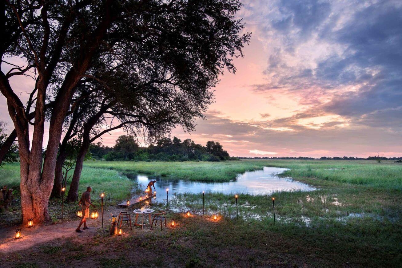 A river and grassy area at sunset with two men setting up lanterns