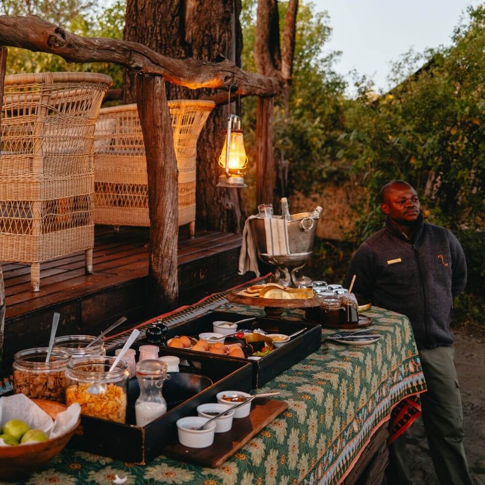 Outdoor table with a breakfast buffet and a staff member standing beside it