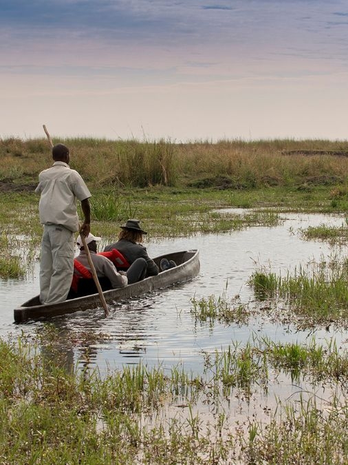 Three people in a mokoro on a grassy waterway