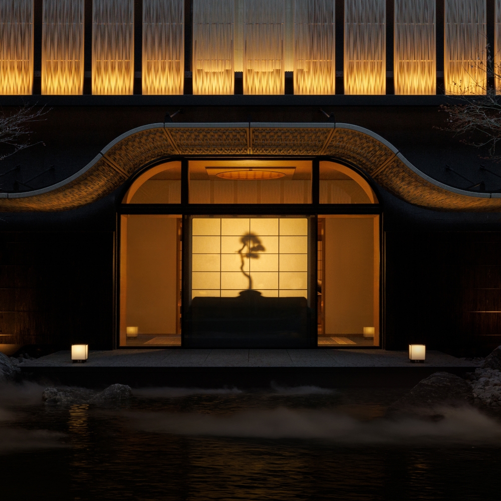 Exterior view of the hotel at night lit from within showing a Japanese screen wall with a bonsai plant illuminated.
