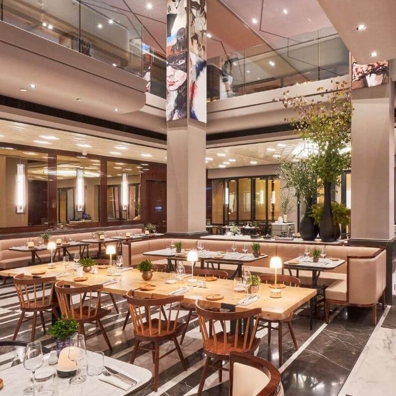 A restaurant with several tables, tiled floors and high ceilings