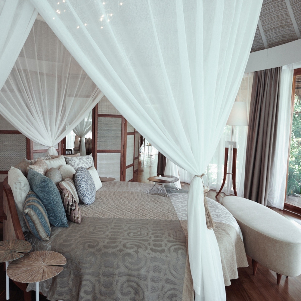 Bedroom with neutral toned bedding surrounded by gathered mosquito nets