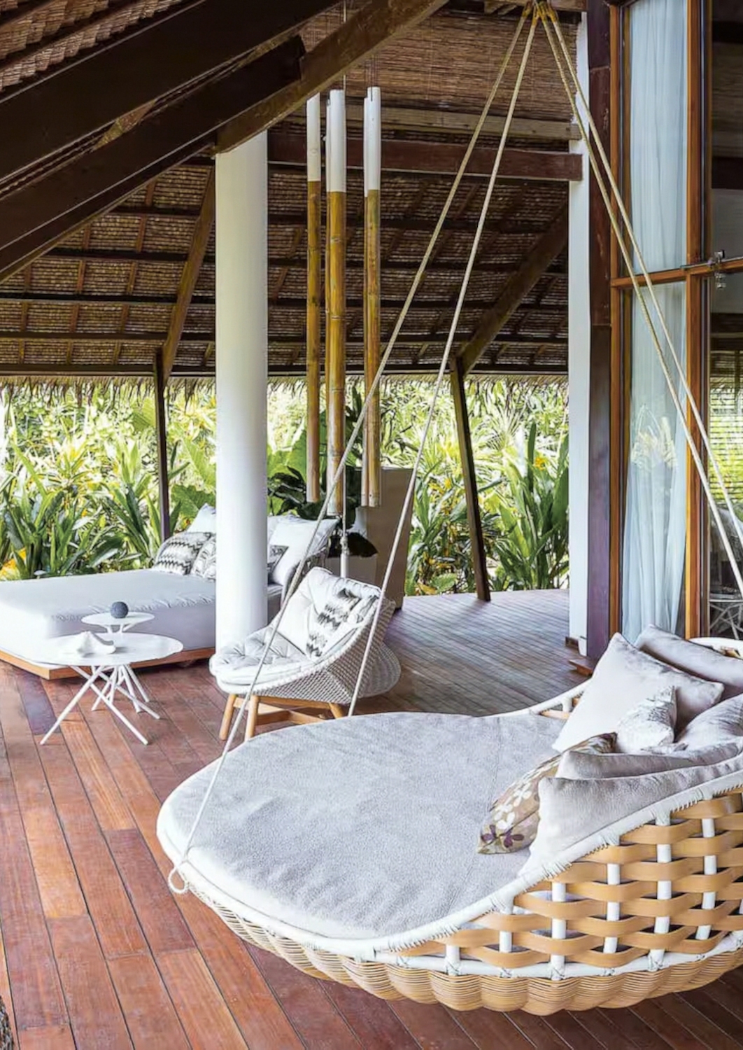 Outdoor room deck with day beds, lounge chairs and swing chairs, with green plants in the background.