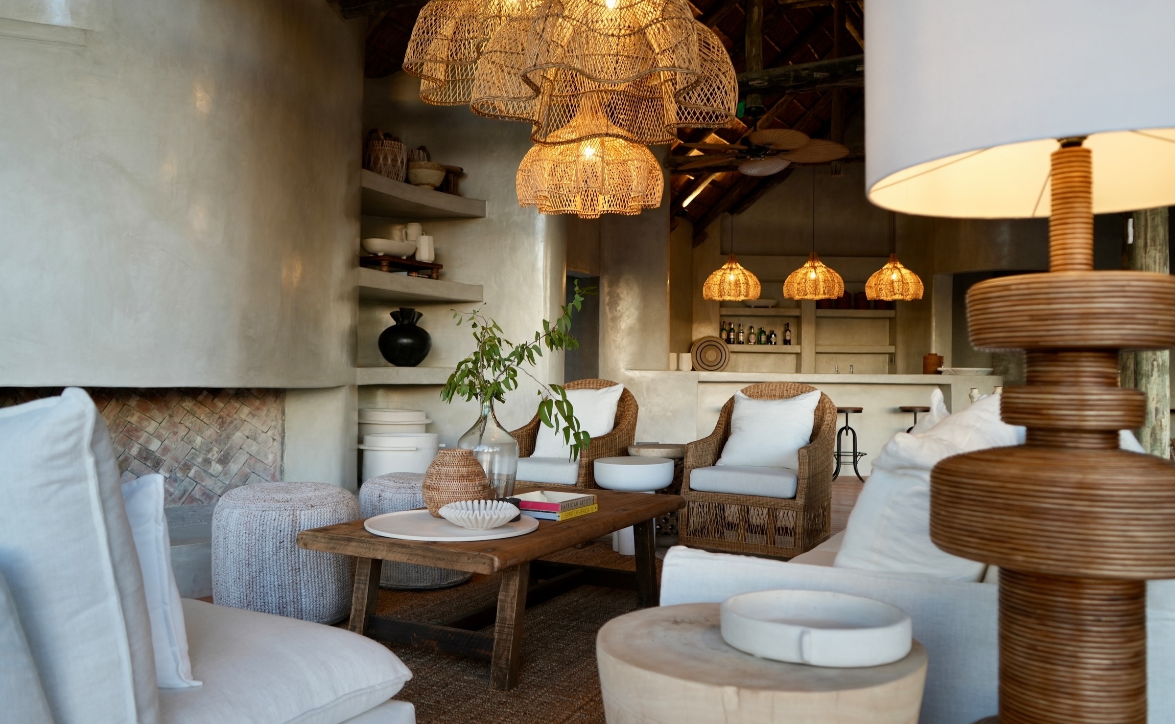 A decorated lounge area at a safari lodge with white sofas, woven chairs, and large woven chandeliers.