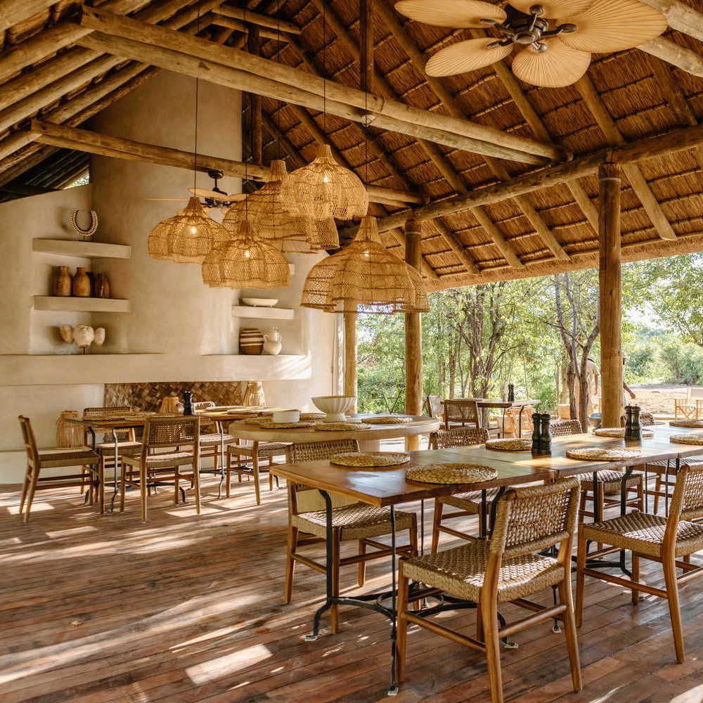 An open-air dining room with a thatched roof, wooden tables and chairs, and large woven pendant lights.