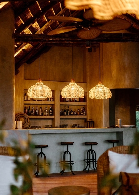 A safari lodge bar with three woven pendant lights illuminating a concrete counter and matching bar stools.
