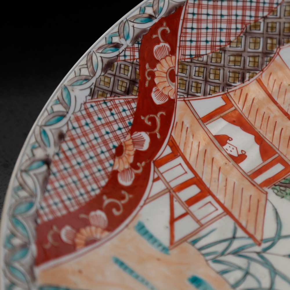 Close-up detail of a painted ceramic plate with traditional Japanese scenes and patterns in red, blue, orange and brown.