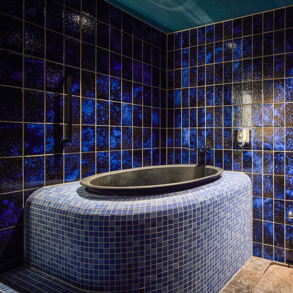 A blue-tiled bathroom with a small, round corner bath.
