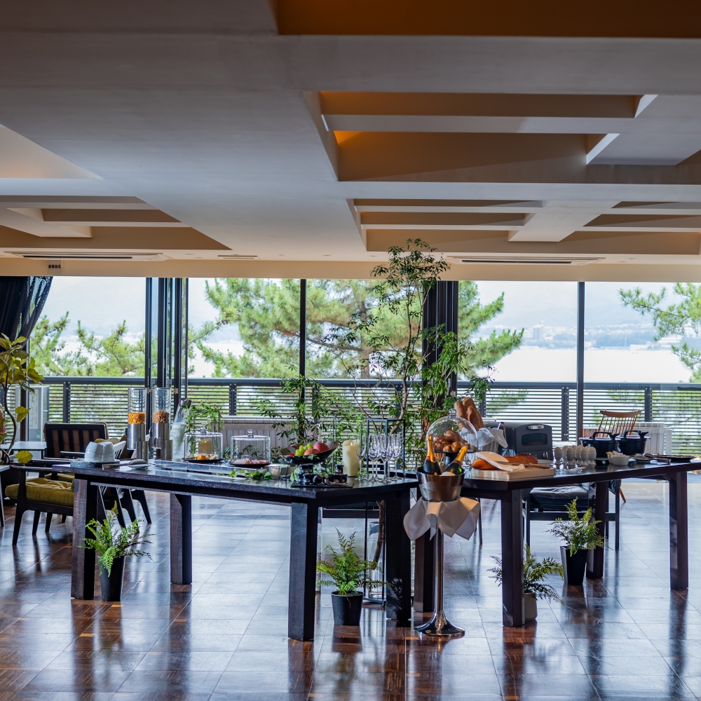 Lounge and dining area with a large table set with buffet-style food and in the background a set of large picture windows overlooking the sea.