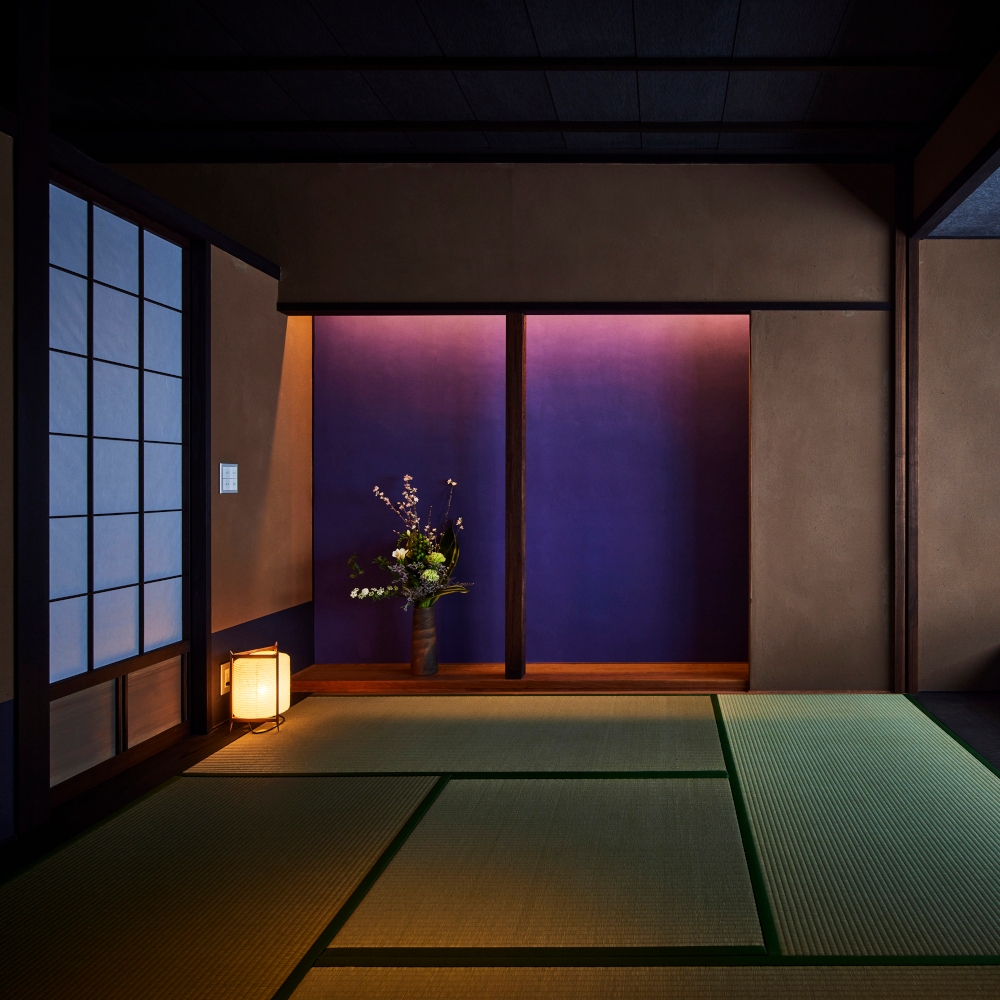 Interior of a traditional Japanese ryokan tatami floor-mat room with small paper lantern on the floor and wooden and paper screens and a colourful purple back wall.