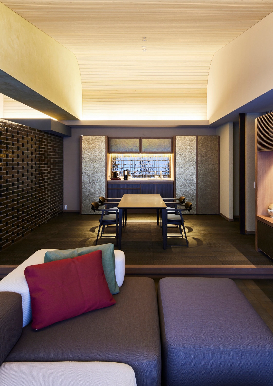 Interior view of a suite's living area with low grey and brown sofas in the foreground and a minimalist table in the background.