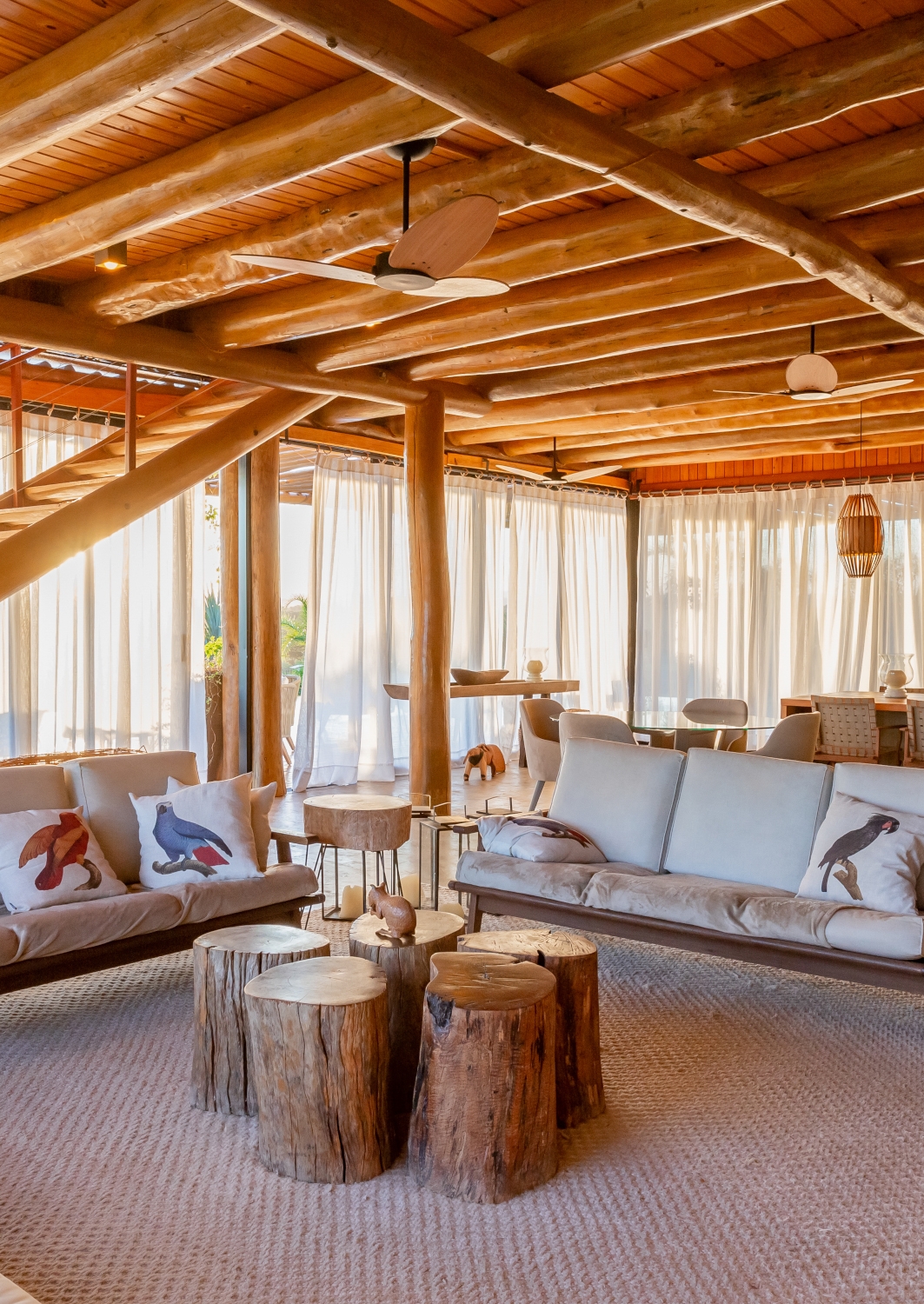 Interior of a villa living area with sofas and ceiling, stairs and pillars made of light wood.