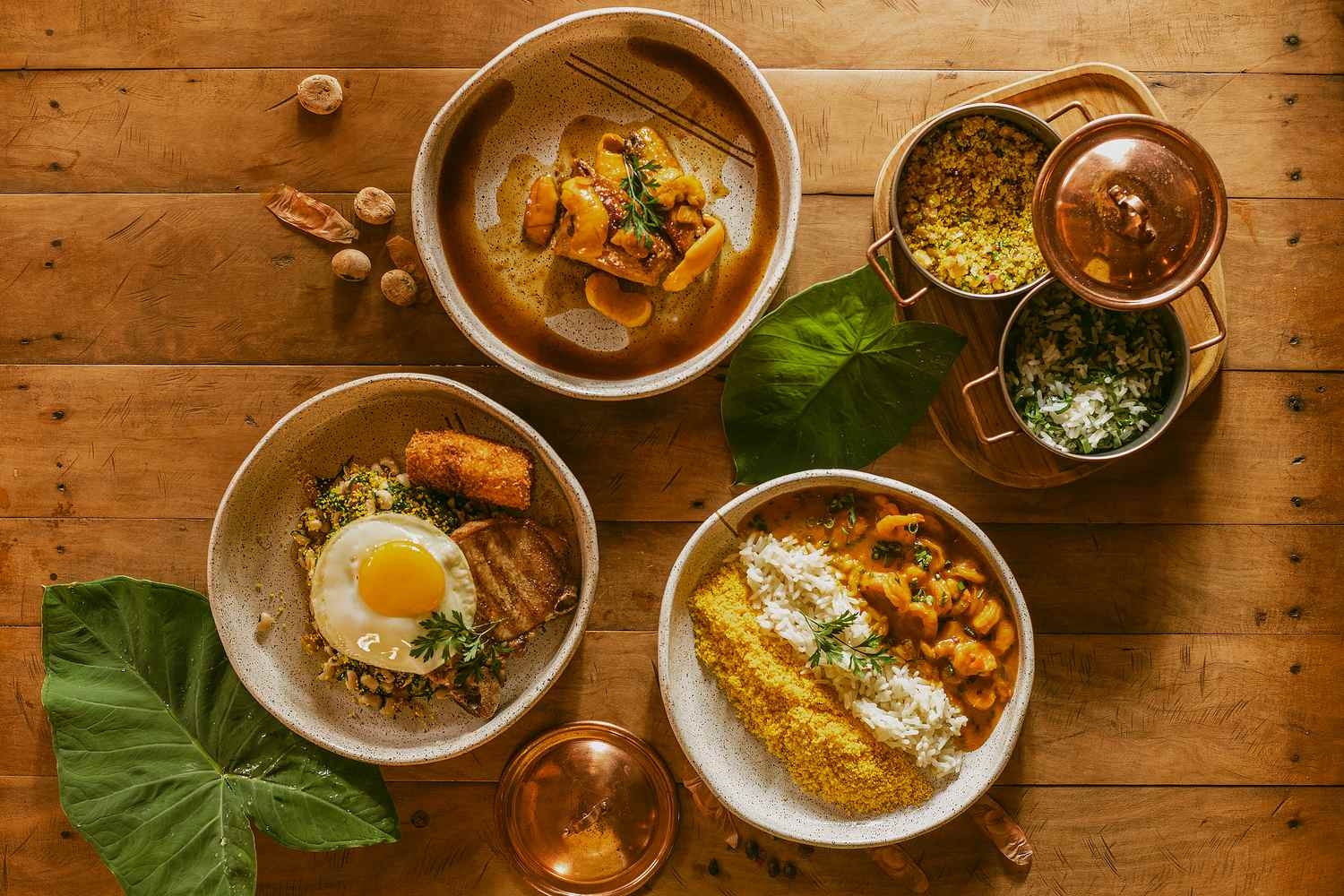 Three bowls with freshly prepared dishes including rice, prawns and a fried egg are laid out on a wooden table.