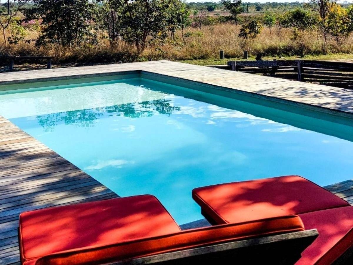 Two red sun loungers in the foreground and a medium-sized outdoor pool surrounded by a wooden deck with views of the Cerrado wilderness.