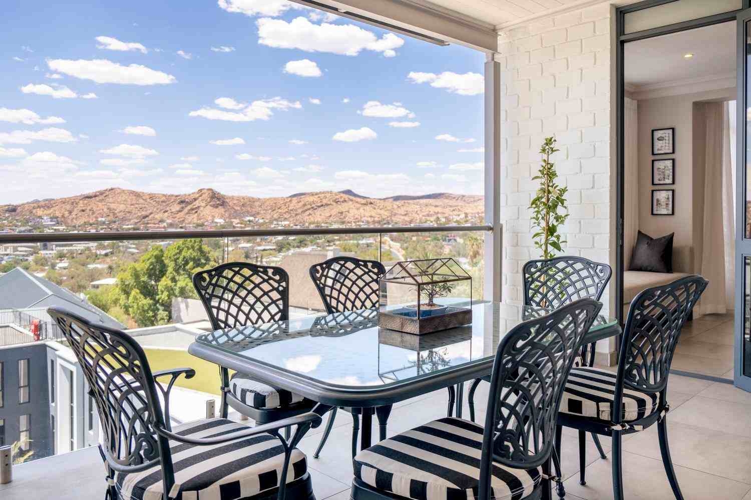 A glass-topped table with eight chairs and a bonsai tree decoration, placed on an open-sided terrace with views of the Auas Mountains