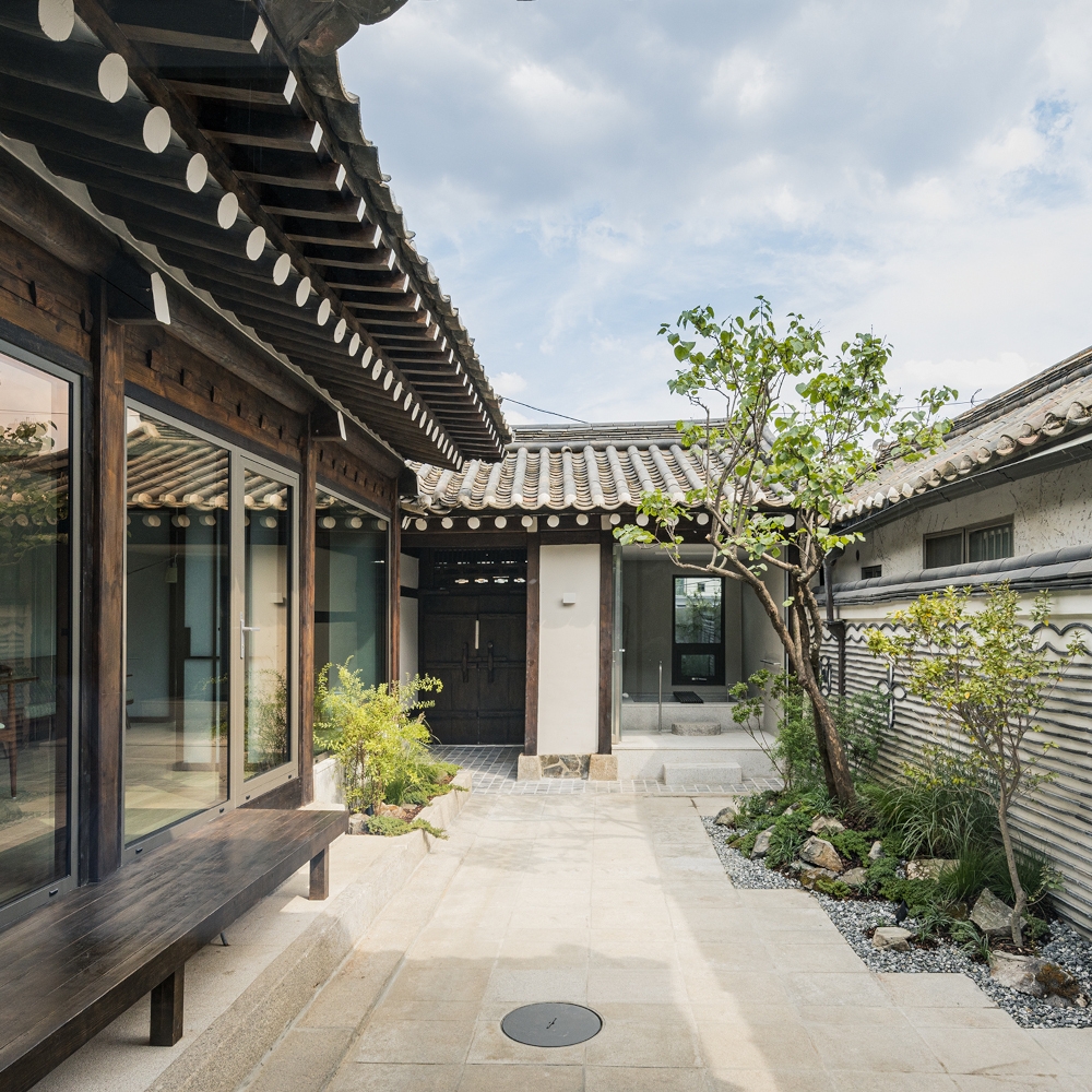 A traditional Korean hanok house in daytime with a tree growing in the centre and floor-to-ceiling windows.