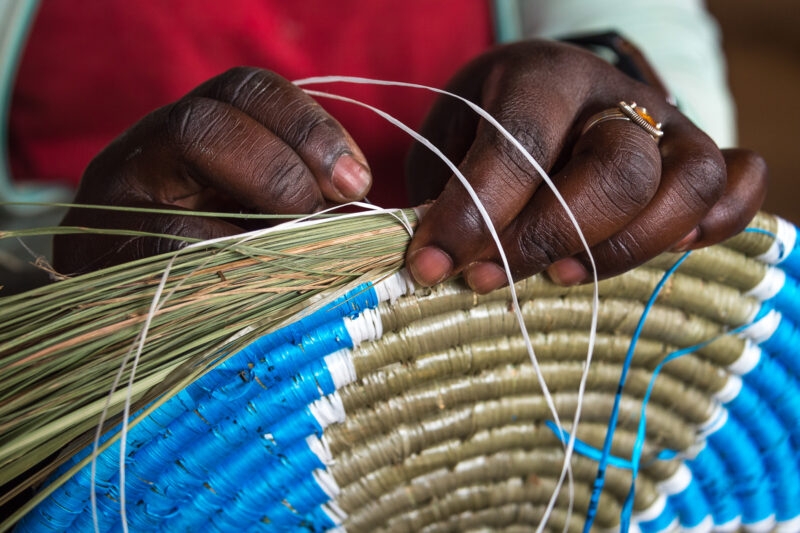 Close-up of hands weaving a colorful basket with natural grass and colored thread. Find cultural immersion on luxury Rwanda vacations.