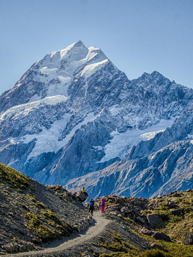 Hikers on a trail below a majestic snow-capped mountain peak on luxury Australasia holidays.