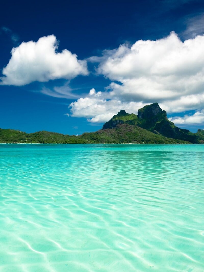 Lush green mountain peak overlooking a turquoise tropical lagoon on luxury French Polynesia tours.