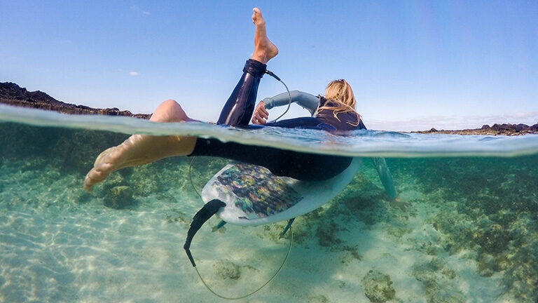 Over under photo of women paddling out on a surfboard