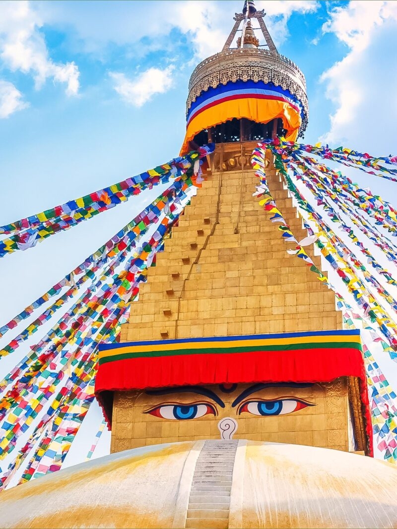 Luxury Asia Tours - Boudhanath Stupa , a colourful temple with golden accents, two blue eyes painted on the front and hundreds of small colourful flags cascading down the side in Kathmandu valley, Nepal