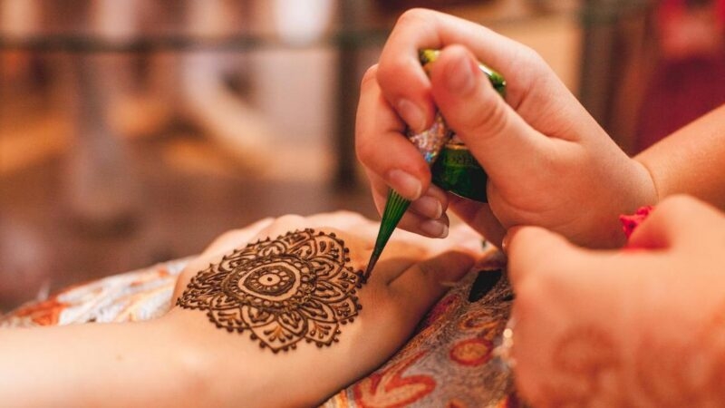 Close up of hands applying an intricate floral henna tattoo design onto a person's palm.