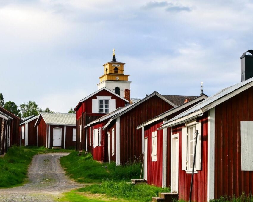 Row of traditional red wooden houses with white trim and a clock tower in the background.