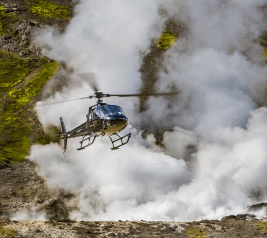 A helicopter flying low over misty, green hillside terrain.