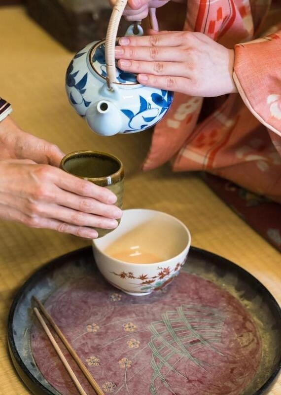 detail of two women in traditional kimono, kneeling on tatami preparing, pouring a cup of tea
