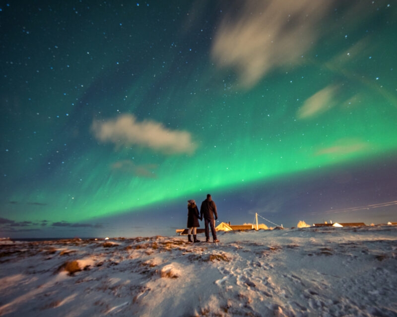 A couple admires the Northern Lights in the mountains of Reine