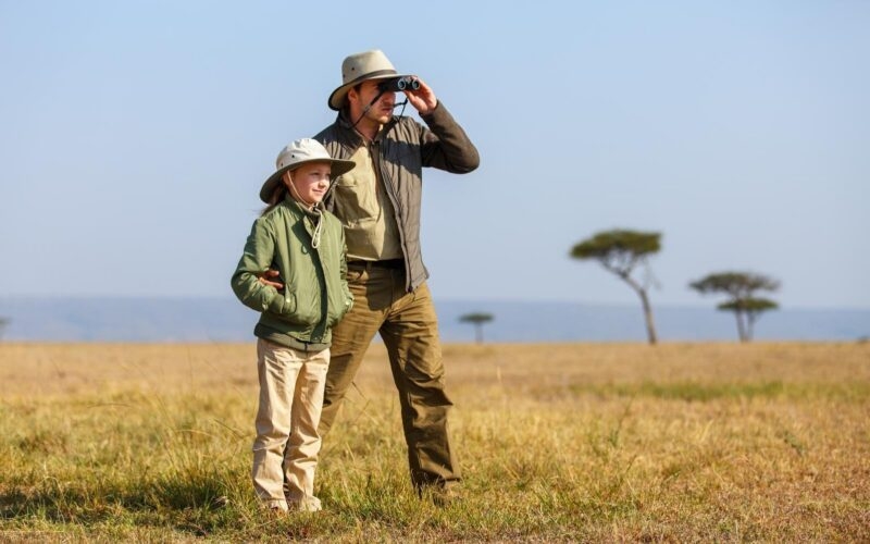 A father and daughter looking through binoculars in the Kenyan savannah