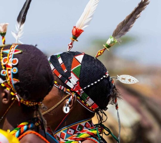 Close-up of people wearing traditional colourful beaded headbands and feathers on their hair.