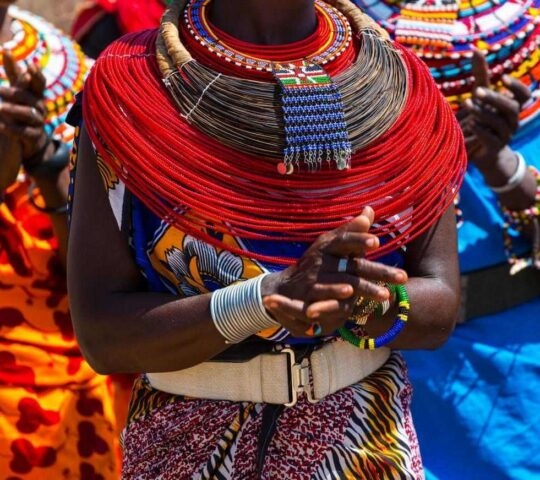 Close-up of vibrant red multi-strand beaded necklaces and traditional clothing worn outdoors.