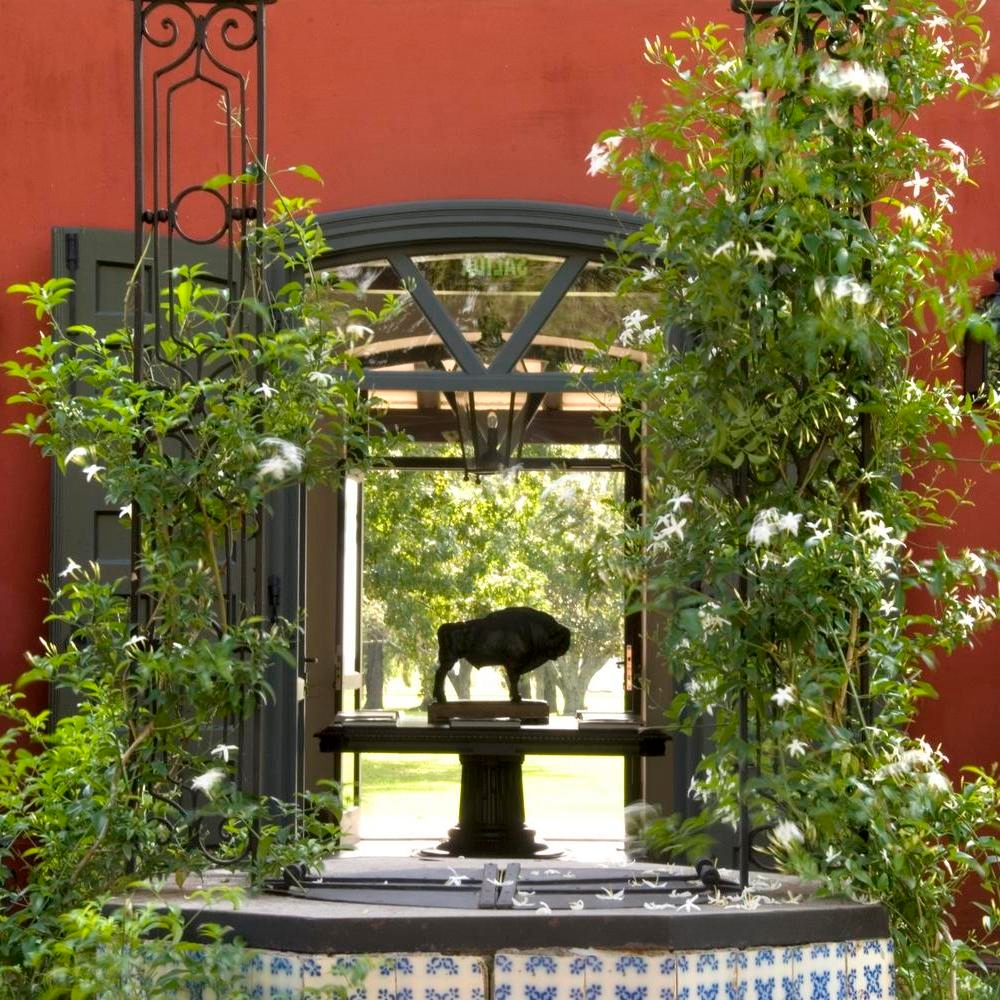 A tranquil garden scene with a buffalo sculpture centered in a doorway, framed by lush greenery and ornate tiles.