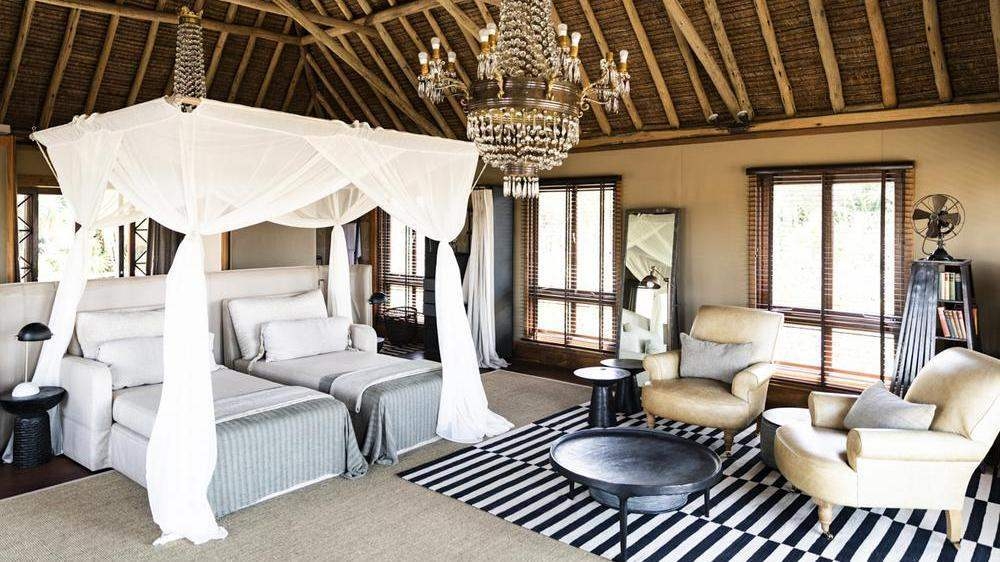 Twin beds with white canopy netting beneath a crystal chandelier, next to a seating area with leather armchairs.