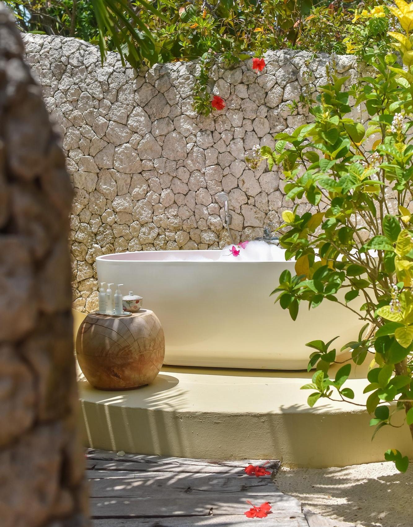 Outdoor bathtub with a stone wall, surrounded by plants and a decorative pot.