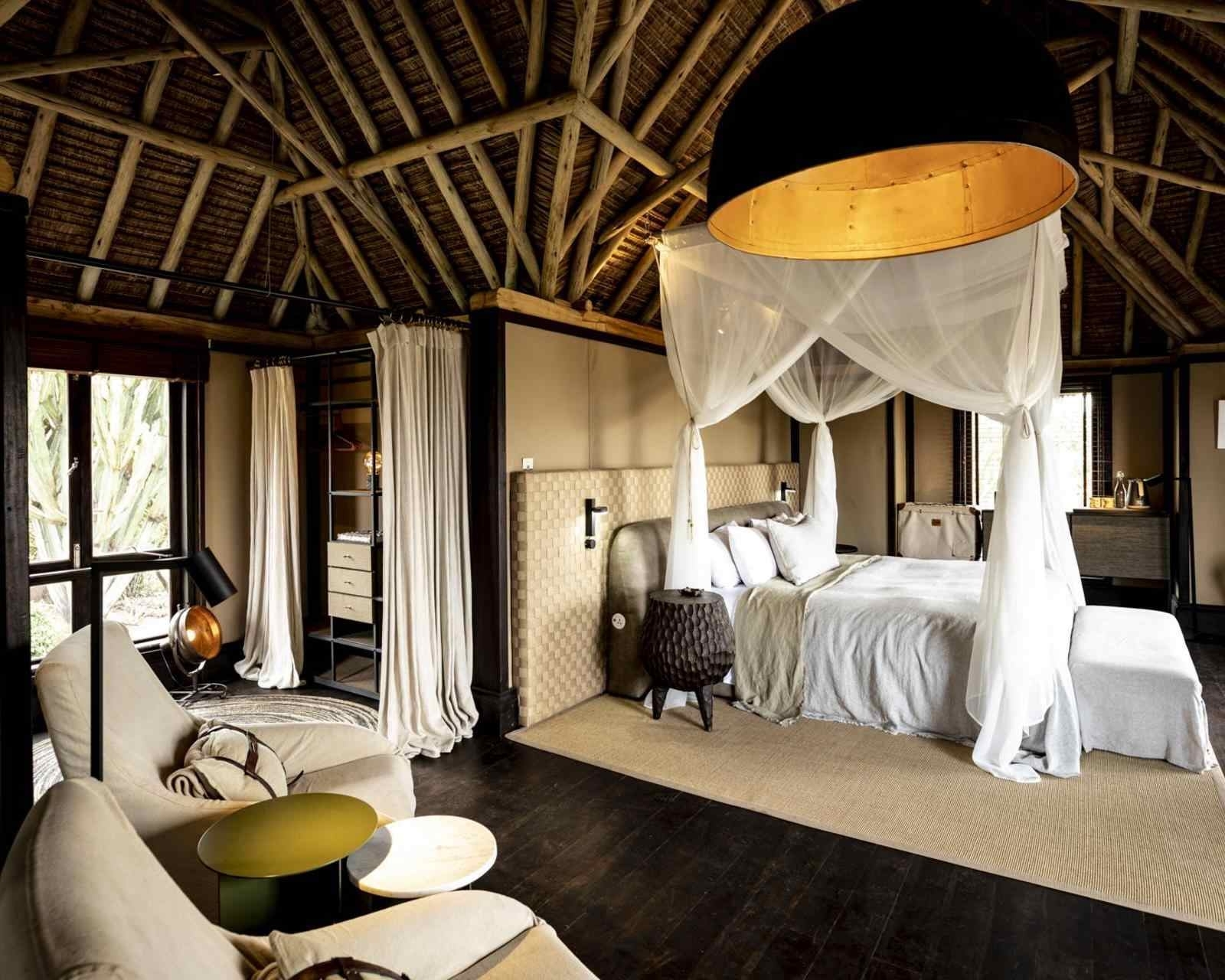 Bedroom inside a villa featuring a canopy bed with white netting, high wooden ceilings, and armchairs.