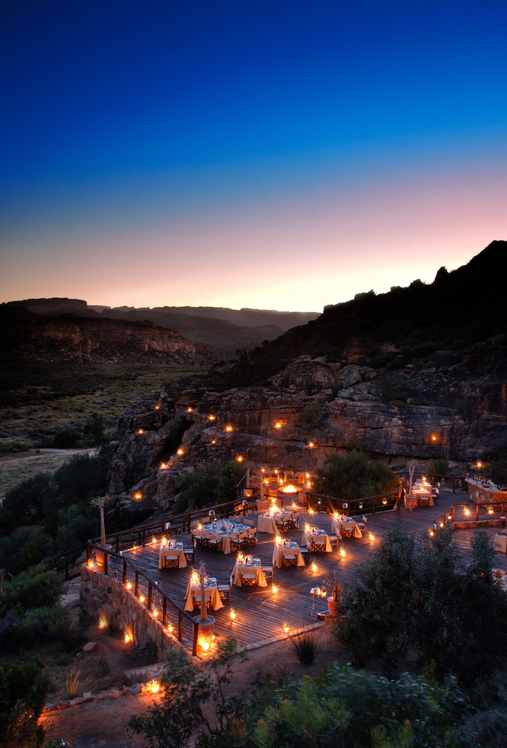 Outdoor dining set up with lights at dusk, nestled in a mountainous area.