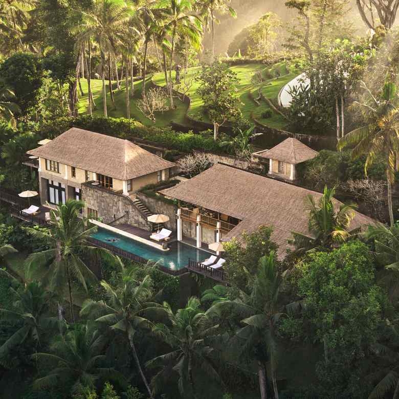 Aerial view of a villa at COMO Shambhala with thatched roofs and a swimming pool nestled in palm trees.