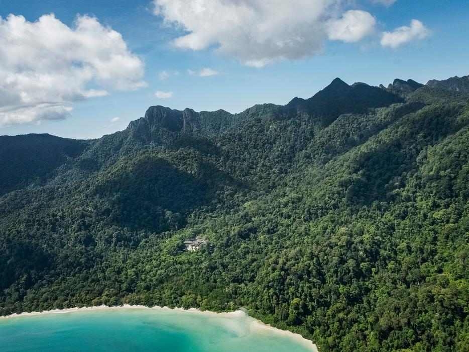 Aerial view of a tropical bay with turquoise water, a white beach and lush green mountains.