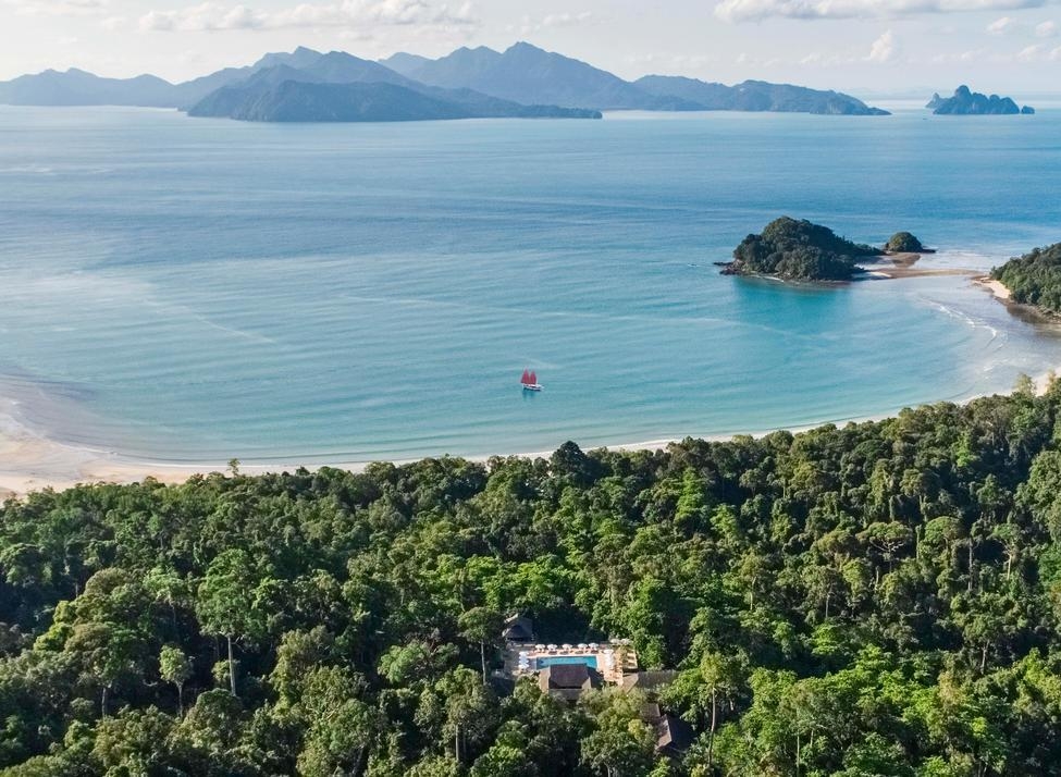Aerial shot of the Datai in the jungle overlooking a wide bay with a sailboat.