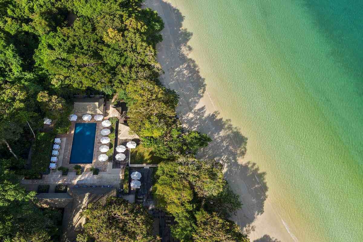 Bird's-eye view of the Datai's pool area located between a dense forest and the ocean shore.
