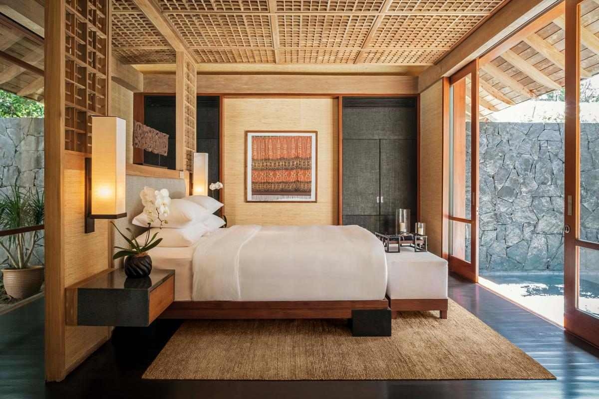 Elegant villa bedroom with a latticed wood ceiling, neutral tones and a view of a stone wall.