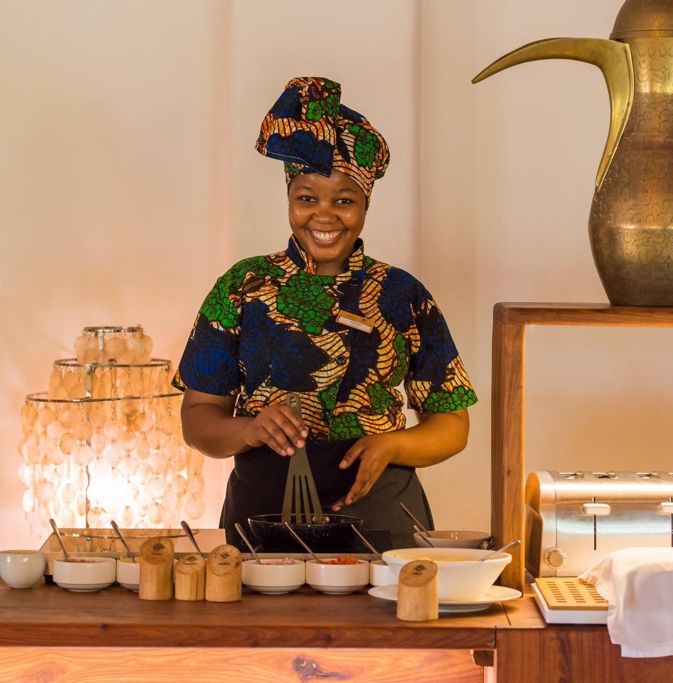 Person in colourful attire prepping food at a buffet station with condiments and utensils.